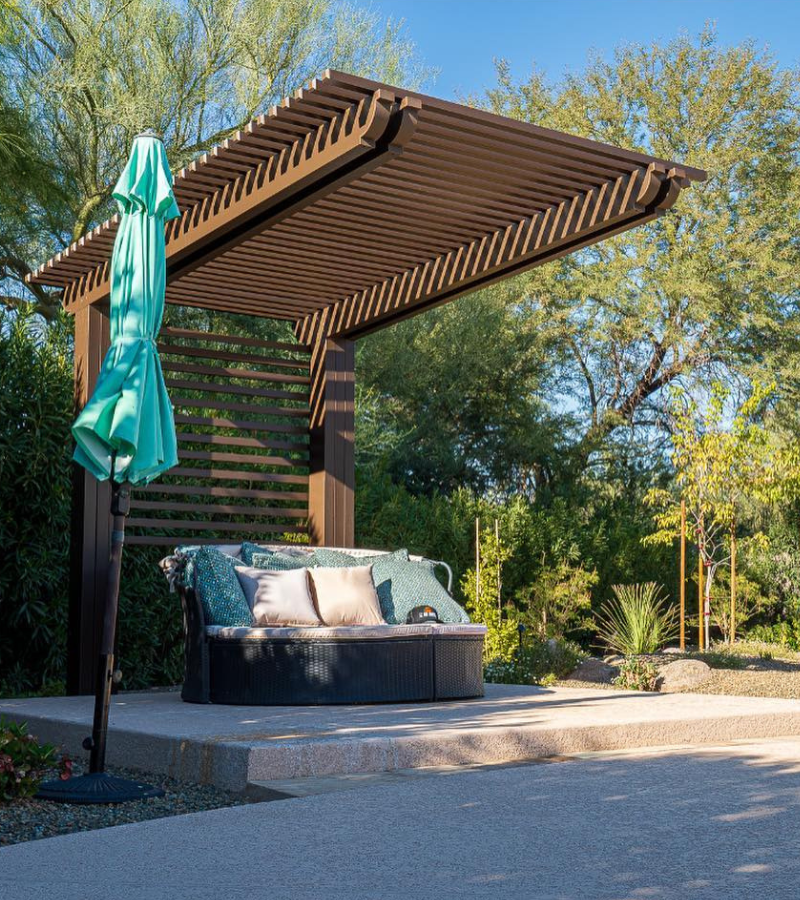 Brown lattice pergola with wicker daybed and desert landscaping